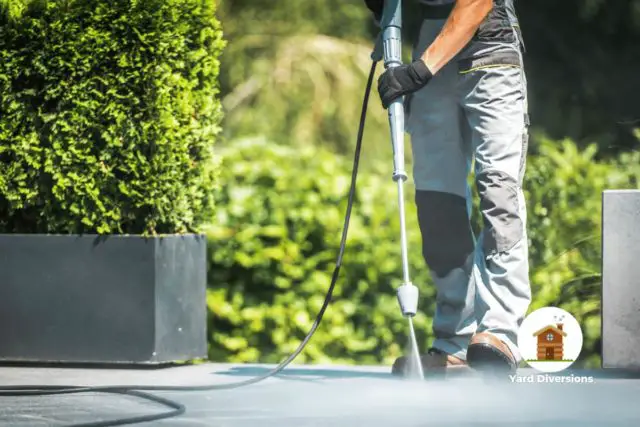 Man pressure washing in pants in the backyard near potted plants