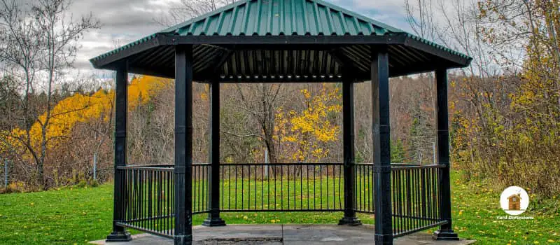 metal gazebo surrounded by grass and woods