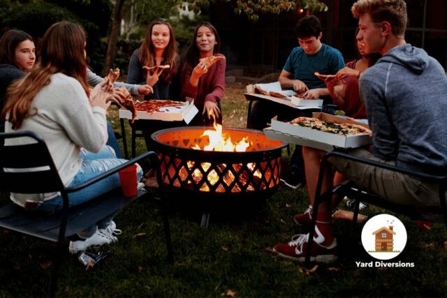 group of college age kids huddled around a late night fire in a fire pit