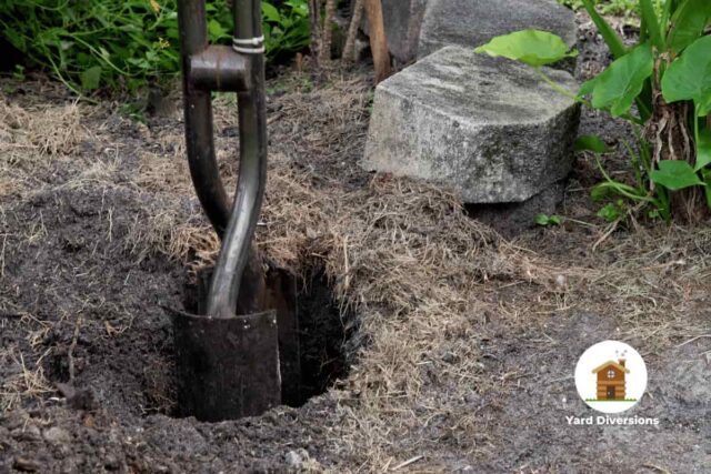 metal post hole digger partially in the ground digging a hole in dirt