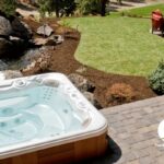 Hot tub on a patio next to waterfalls and a nice grass area with a full patio furniture set