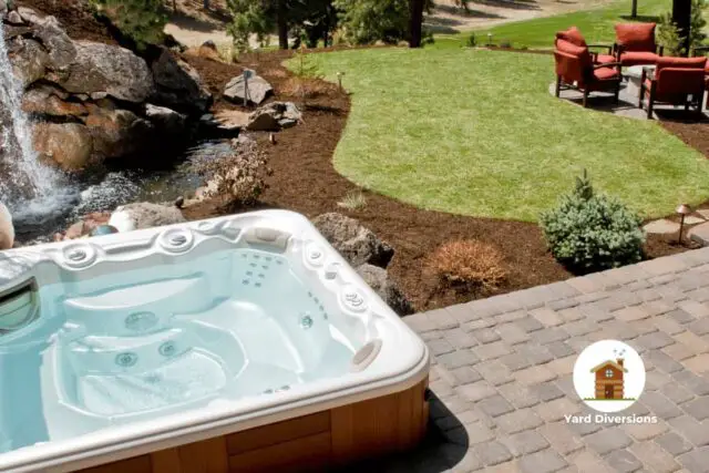 Hot tub on a patio next to waterfalls and a nice grass area with a full patio furniture set