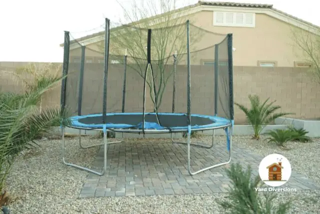 Trampoline with a net setup on patio pavers and gravel