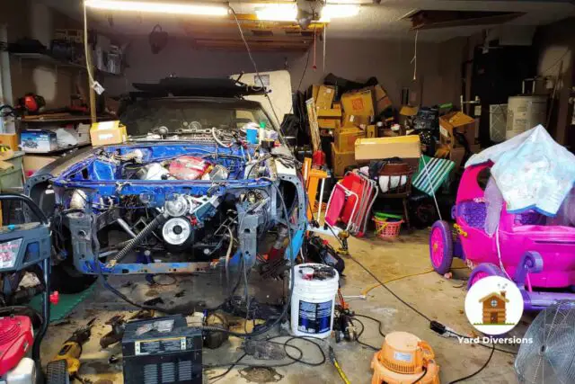 A very messy and cluttered garage with a partly dismantled car and stuff strewn all around