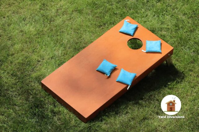 Brown wooden cornhole board with four blue bean bags on it