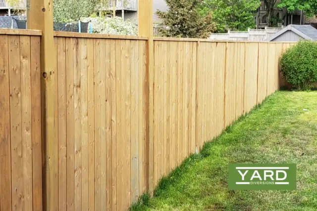 A tall, wooden privacy fence in a backyard, with lush green grass running alongside it. The logo "Yard Diversions" is visible in the bottom right corner of the image.